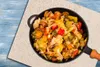 A close-up overhead shot of a pan filled with mixed vegetables, placed on a textured surface with a blue wooden background. Náhľad obrázku produktu