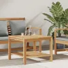 A wooden coffee table is placed on a patio next to outdoor seating, with a plant in the background. Náhled obrázku produktu