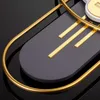 A close-up shot of a modern wall clock with a dark gray face and gold accents, set against a black reflective surface. Produktbild-Vorschau