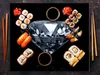 A flat lay of sushi and a large diamond on a dark background, with chopsticks and soy sauce dishes. Náhľad obrázku produktu