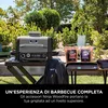 A Ninja Woodfire grill and accessories are set up outdoors in a garden setting. Náhľad obrázku produktu