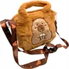 A fluffy brown handbag with a capybara design and a patterned strap. Produktbild-Vorschau