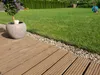 A garden scene with a wooden deck, a potted plant, and a lawn. Anteprima dell’immagine prodotto