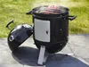 A black charcoal smoker grill with its lid open, showing food cooking inside, placed on a patio with grass in the background. Produktbild-Vorschau