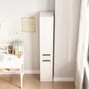 A tall, narrow white cabinet with two drawers is shown next to a desk with books and art supplies. Podgląd zdjęcia produktu