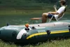 An inflatable boat is in the foreground on grass, with a person sitting in a chair in the background near a body of water. Podgląd zdjęcia produktu