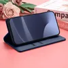 A blue phone case with a phone inside, placed on a pink surface with some flowers in the background. Produktbild-Vorschau