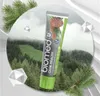 A tube of toothpaste is shown against a backdrop of a misty forest and mountains, with pine branches and geometric shapes around it. Voir les images du produit