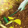 A gloved hand is using a small green rake to tend to plants in a garden. Podgląd zdjęcia produktu