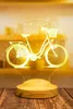 A 3D LED lamp shaped like a bicycle with a basket, placed on a wooden base. Produktbild-Vorschau