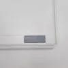 A close-up view of the bottom edge of a white drawing board with a gray accessory attached to the frame. Náhľad obrázku produktu
