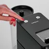 A close-up shot of a hand pressing a button on a black coffee machine. Náhľad obrázku produktu