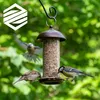 A bird feeder filled with seeds, with three birds feeding from it in a natural, leafy environment. Produktbild-Vorschau