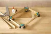 A wooden frame is being assembled on a wooden surface using corner clamps, glue, and a ruler. Produktbild-Vorschau