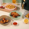A collection of air fryer silicone liners filled with food, placed on a table next to an air fryer. Produktbild-Vorschau