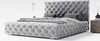 A tufted grey upholstered bed with pillows and a bedside table with a vase and a lamp. Náhled obrázku produktu