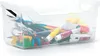 A clear plastic storage bin filled with art supplies like pencils, crayons, and tubes of paint. Anteprima dell’immagine prodotto