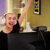 A person wearing headphones is celebrating in front of a computer screen with a webcam attached. Produktbild-Vorschau