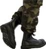 A close-up shot of a person wearing camouflage pants and black combat boots. Produktbild-Vorschau