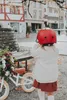 A young child wearing a red helmet stands next to a balance bike decorated with festive greenery and berries. Produktbild-Vorschau