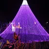 A large, cone-shaped Christmas tree decorated with numerous purple lights, with a white top. There are also decorative figures of a giraffe and people on the tree. The base of the tree is also illuminated with colorful lights. Produktbild-Vorschau
