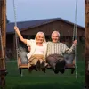 An elderly couple sits on a swing in front of a house. Podgląd zdjęcia produktu