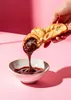 A hand holding a croissant filled with chocolate spread, dipping it into a bowl of chocolate spread against a pink background. Produktbild-Vorschau