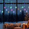 A cozy living room scene with a couch and pillows, viewed through a window decorated with snowflake string lights, overlooking a snowy forest and a Christmas tree. Náhled obrázku produktu