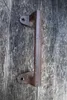 A close-up shot of a rustic, cast iron door handle attached to a weathered wooden door. Produktbild-Vorschau