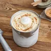 An ice cream maker container filled with ice cream, drizzled with caramel and sprinkled with nuts, placed on a wooden table. Produktbild-Vorschau