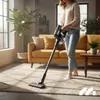 A woman is vacuuming a rug in a living room with a sofa and a plant. Podgląd zdjęcia produktu