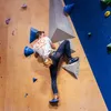 Kletterer in blauer Hose und weißem T-Shirt mit Logo von YY Vertical; der an einer Kletterwand mit verschiedenen Griffen klettert. Er trägt einen Chalk Bag in Form eines Faultiers. Produktbild-Vorschau