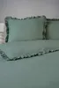 A close-up view of a bed with mint green bedding and ruffled pillowcases. Produktbild-Vorschau