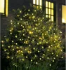 A bush decorated with warm white LED lights at night, with a brick building and windows in the background. Produktbild-Vorschau