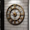A large, vintage-style metal wall clock with Roman numerals is mounted on a brick-patterned wall. Produktbild-Vorschau