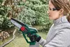 A woman is using a cordless chainsaw to trim branches outdoors. Produktbild-Vorschau