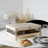 A wooden cheese cellar with a glass lid sits on a white table, with a loaf of bread and a plate in the foreground. Voir les images du produit