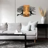 A metal wall art piece depicting two tree-like faces looking at each other, mounted on a wooden panel, above a sofa in a living room. Produktbild-Vorschau