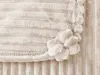A close-up view of a beige blanket with a textured stripe pattern and a decorative flower embellishment. Náhled obrázku produktu