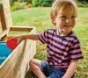 A young boy is playing with a red ball next to a wooden structure in a grassy yard. Náhled obrázku produktu