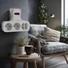 A white power strip with a red switch is mounted on a gray wall, with a chair and plants in the background. Produktbild-Vorschau