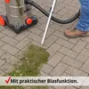A person is using a wet/dry vacuum cleaner to clean up grass clippings from a paved patio. The vacuum cleaner is silver with orange accents and black wheels. The hose and wand are attached, and the wand is near the grass. Produktbild-Vorschau