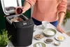 A person is adding ingredients to a bread maker, with various baking ingredients laid out on a counter. Náhľad obrázku produktu