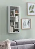 A white modern wall shelf filled with books and decorative items, mounted on a light green wall above a gray sofa. Produktbild-Vorschau