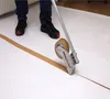 A person is using a tape dispenser to apply brown tape to a white surface, possibly flooring or a protective covering. Produktbild-Vorschau