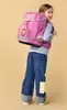 A young girl wearing a pink backpack and jeans, looking over her shoulder. Voir les images du produit