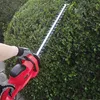 A person is using an electric hedge trimmer to trim a green bush. Produktbild-Vorschau