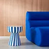 A blue striped side table next to a blue sofa against a wood-paneled wall. Produktbild-Vorschau