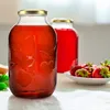 Two glass jars filled with red liquid, one with embossed fruit designs, and a bowl of strawberries in the foreground. Podgląd zdjęcia produktu