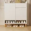 A white shoe cabinet with wooden legs, displaying shoes on its shelves. Náhľad obrázku produktu